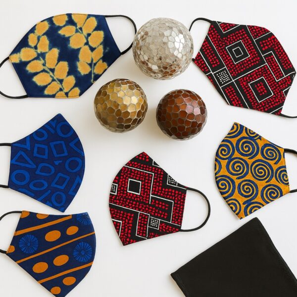 Studio product photo of a single Ankara face mask with bold orange and blue dotted lines and radial motifs. Side view with black earloop, white background.