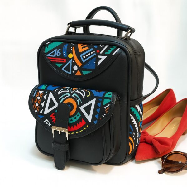 Black leather backpack with colorful Ankara patterns beside red flats and sunglasses in a bright studio setting.