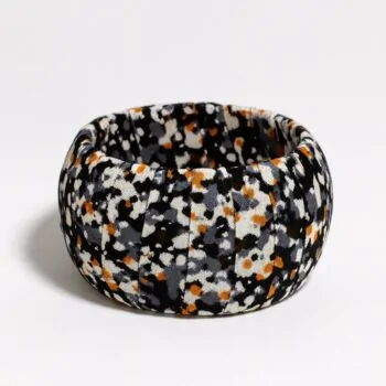 Ankara print bangle with abstract black, white, orange, and gray speckles on fabric, shot on a white background.