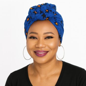 Woman wearing a blue Ankara headwrap with black and orange star patterns, smiling.