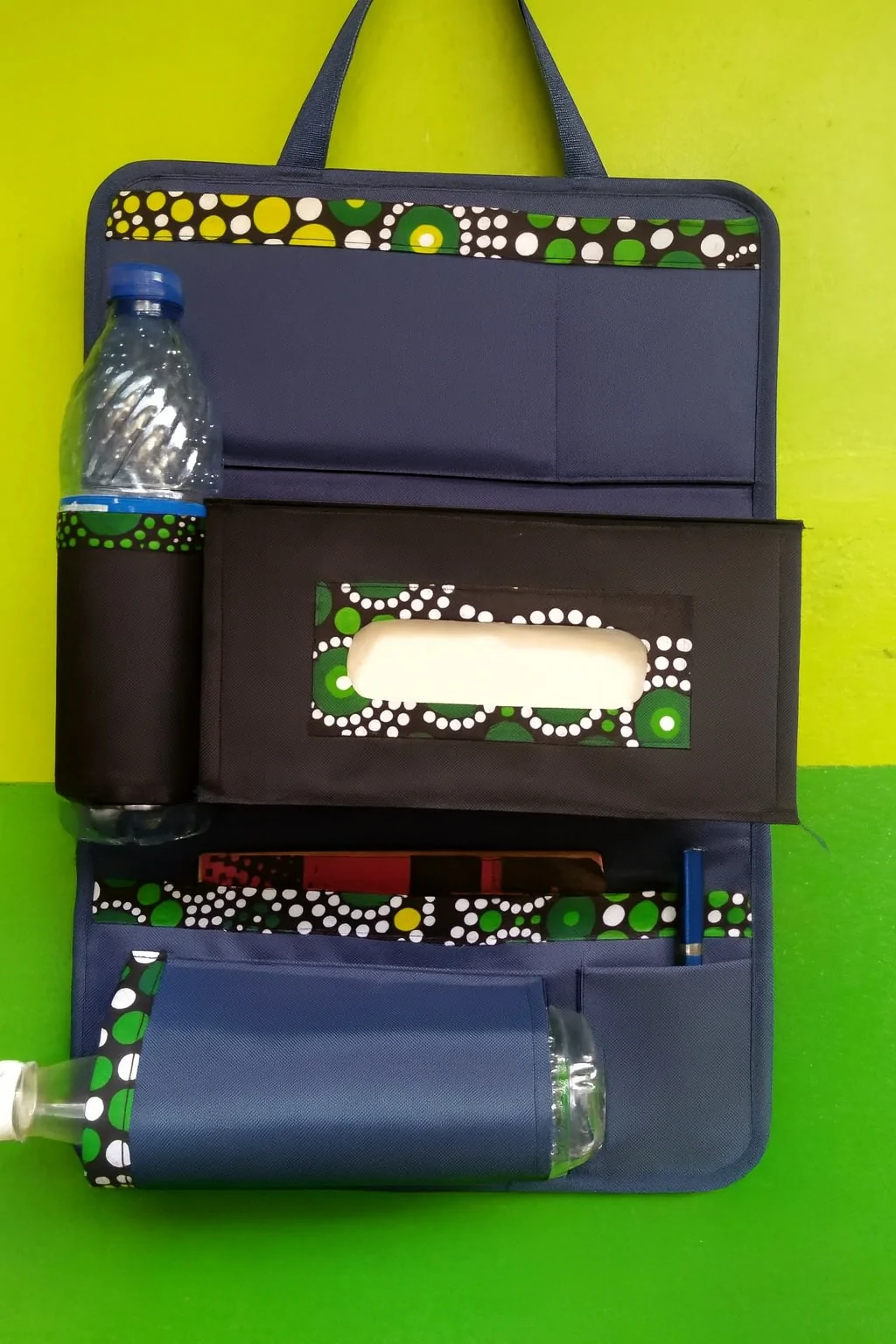 Colorful African-inspired backseat organizer with black tissue box and multiple storage pockets, styled with green and white Ankara trim.