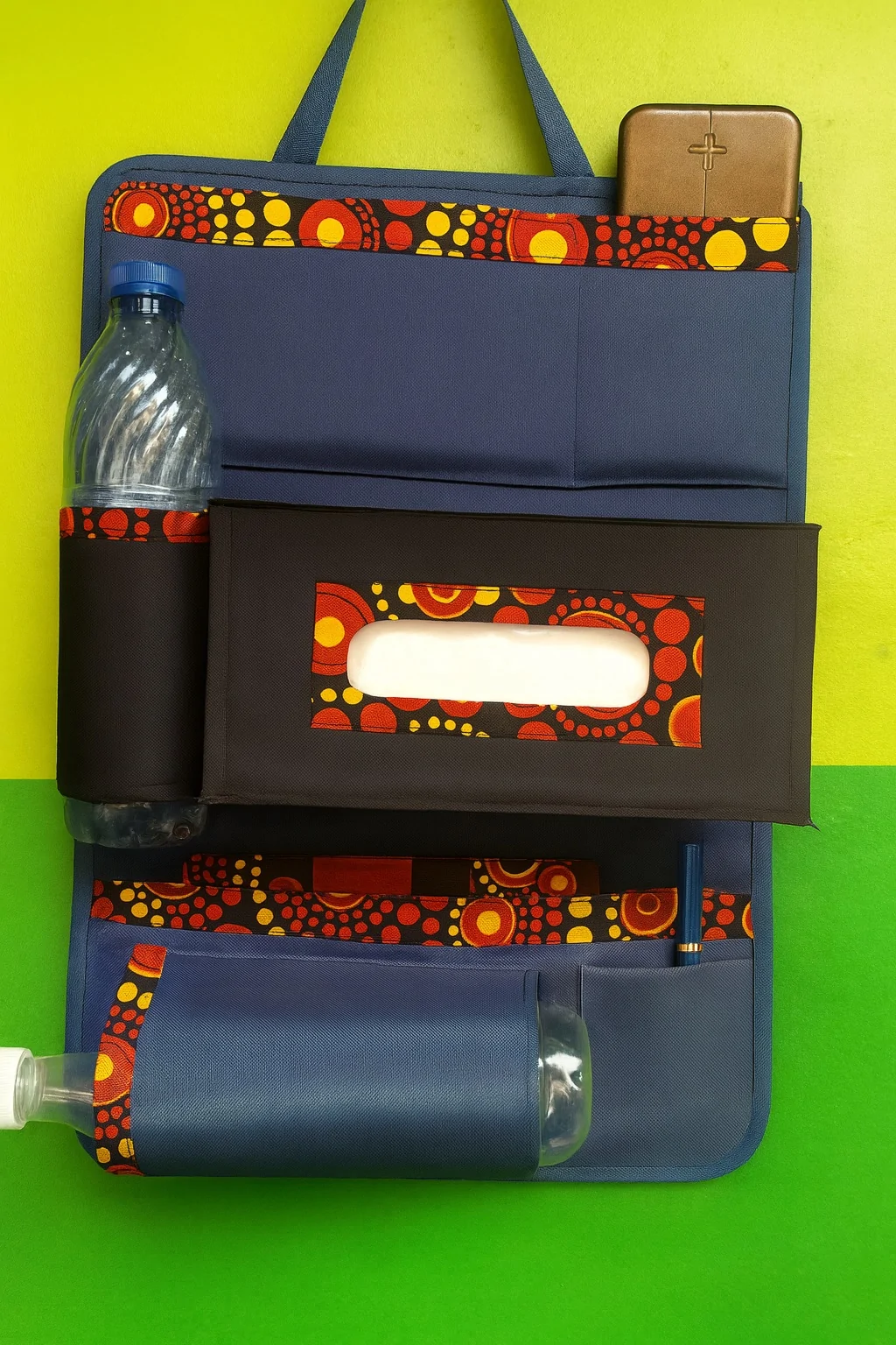 Vibrant Ankara print car seat organizer with bold red and yellow circle patterns, fitted with bottle holder and tissue compartment.