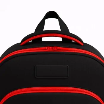 Close-up of the top handle and zipper section of a durable black customizable school backpack with red trim, showing reinforced stitching and double zipper design.