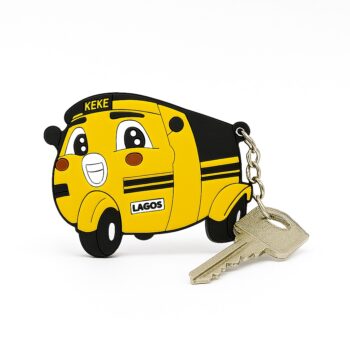Yellow and black PVC Naija Keke cartoon keyholder with cheerful facial features and labeled “LAGOS”, attached to a silver metal keyring holding a house key.