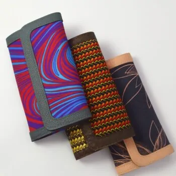 Three African print Ankara ladies' purses – assorted patterns in vibrant colors, each with a leather trim, arranged overlapping on a white background.