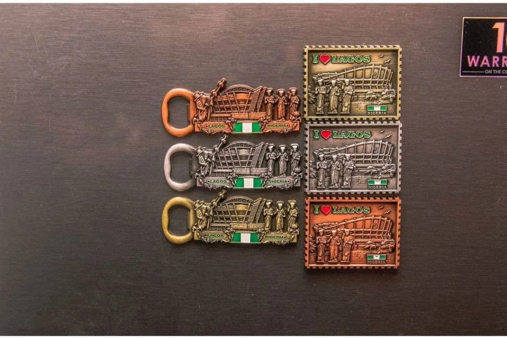 Gold, silver, and orange colored Nigeria tourism fridge magnet.