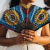Close-up shot of a bride's hands holding a single, beautifully crafted Ankara hand fan.