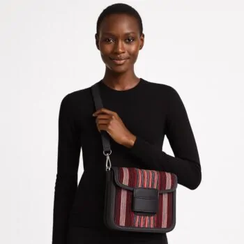 Confident African woman in a black sweater showcasing a red-striped Aso Oke side bag worn on the shoulder.