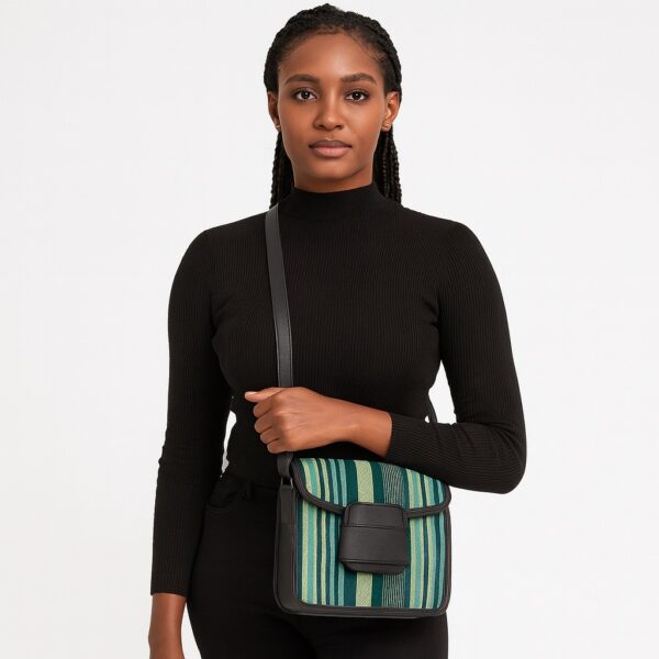 Beautiful African woman in black holding a green-striped Aso Oke side bag with black leather flap and crossbody strap.