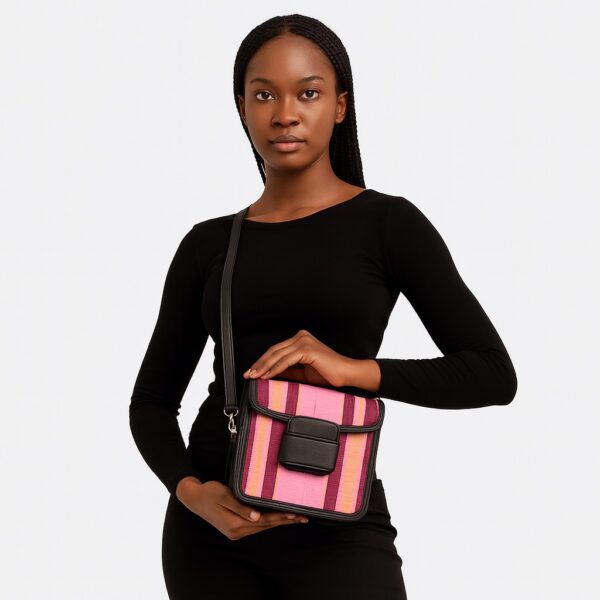 Stylish African woman in black top posing with a vibrant pink and purple Aso Oke side bag, held at waist level.