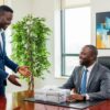 Two Nigerian men in an office, one presenting a gift to his male boss.