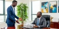 Two Nigerian men in an office, one presenting a gift to his male boss.