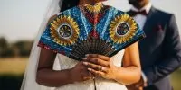 Close-up shot of a bride's hands holding a single, beautifully crafted Ankara hand fan.