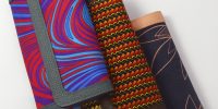 Three African print Ankara ladies' purses – assorted patterns in vibrant colors, each with a leather trim, arranged overlapping on a white background.